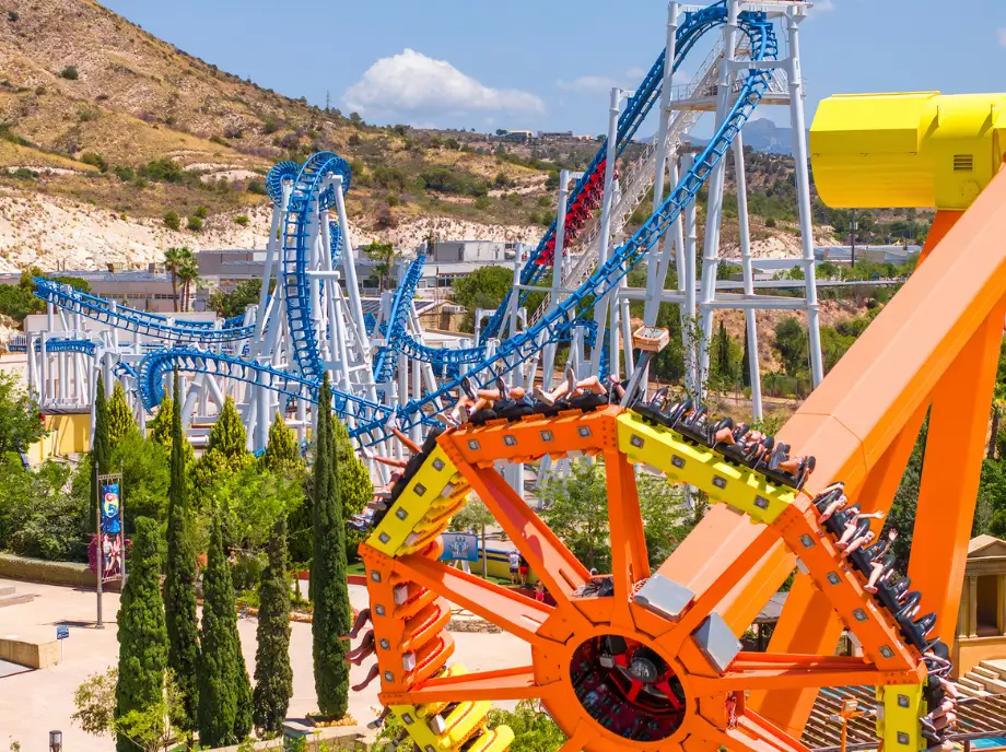Manèges mécaniques et montagnes russes à Terra Mitica Benidorm entourés de verdure.